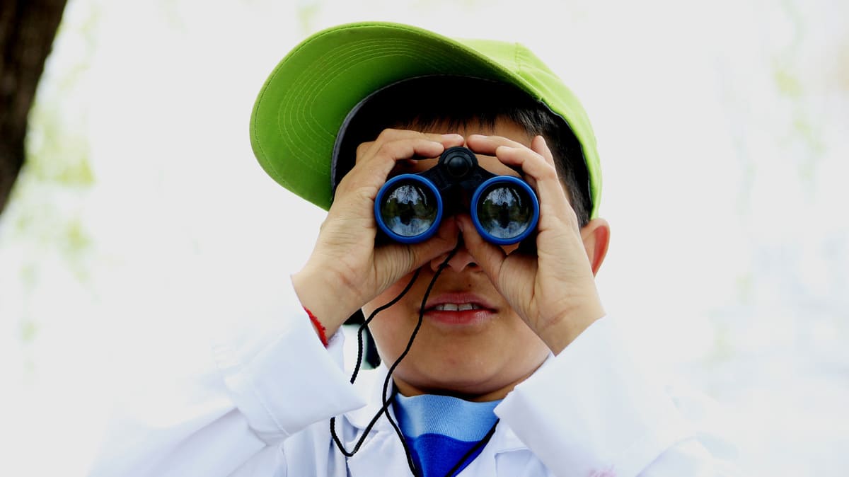 Niño observando a través de binoculares, mirando directamente a la cámara.